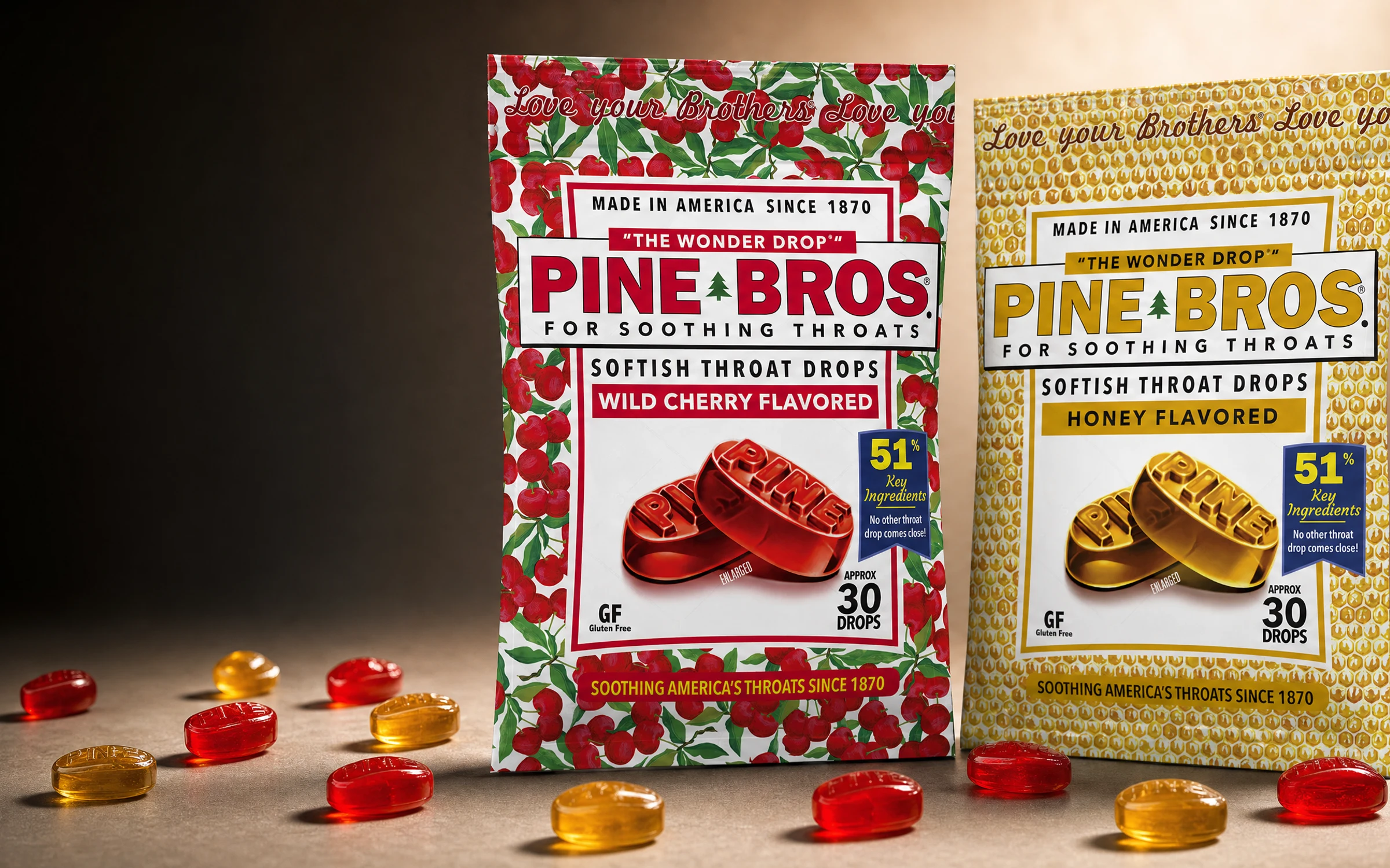 Pine Bros Wild Cherry and Real Honey multipacks standing upright with loose translucent throat drops scattered around them